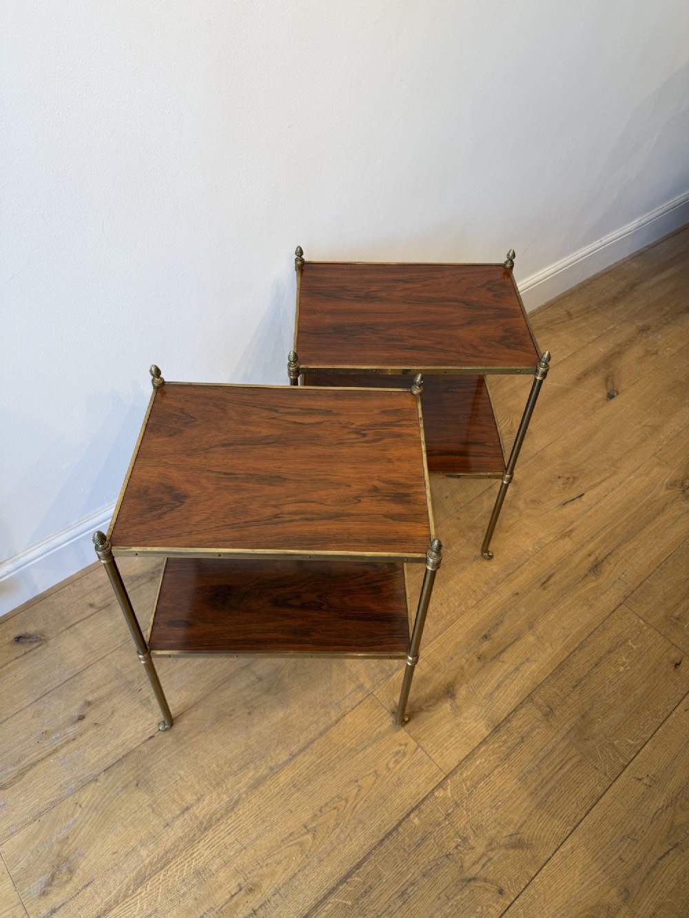 A pair of two-tier brass side tables featuring dark polished wood shelves, finial tops, and slender legs with small castors. View VI