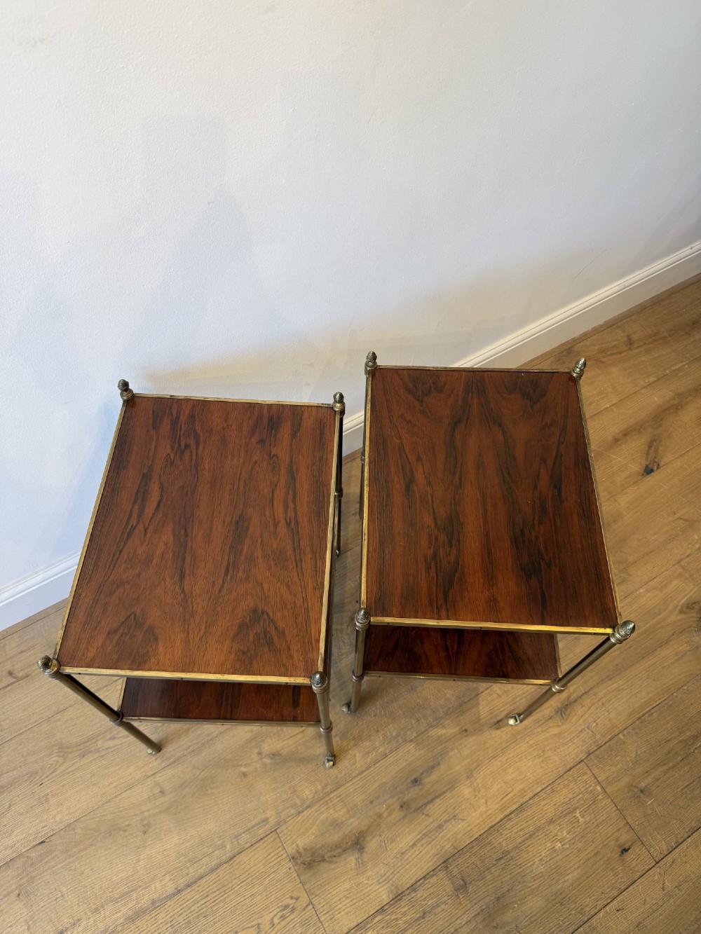 A pair of two-tier brass side tables featuring dark polished wood shelves, finial tops, and slender legs with small castors. View VII