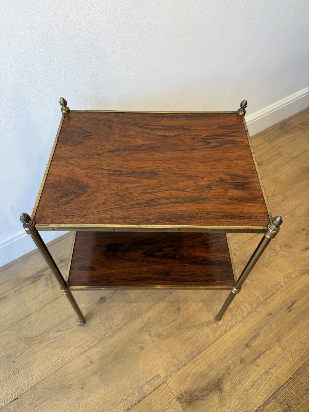 A pair of two-tier brass side tables featuring dark polished wood shelves, finial tops, and slender legs with small castors. View VIII