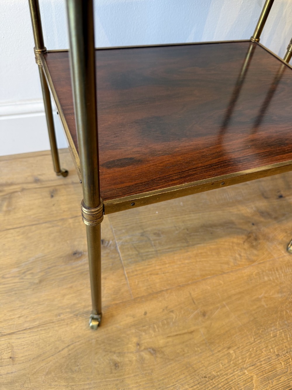 A pair of two-tier brass side tables featuring dark polished wood shelves, finial tops, and slender legs with small castors. View X