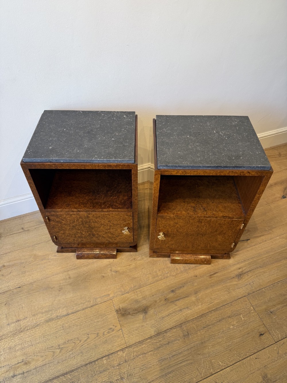 A pair of Art Deco burr walnut bedside cabinets featuring dark stone tops, open upper shelves, and single cupboard doors with square metal handles. View II