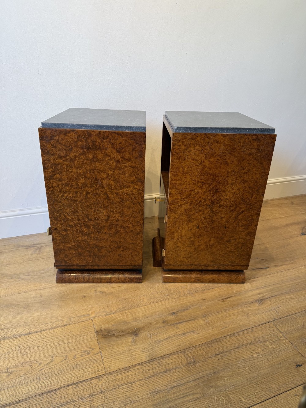 A pair of Art Deco burr walnut bedside cabinets featuring dark stone tops, open upper shelves, and single cupboard doors with square metal handles. View IV