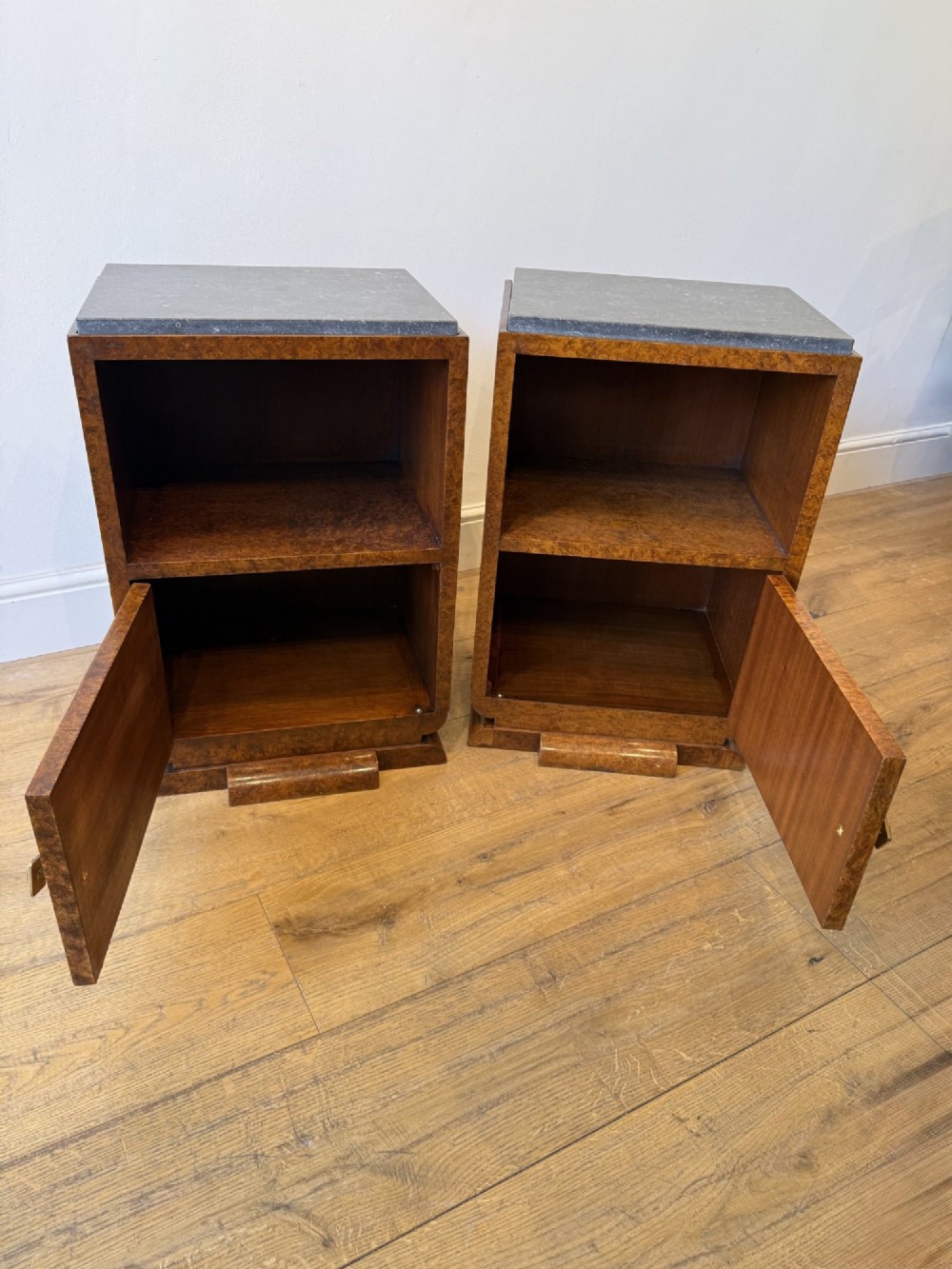 A pair of Art Deco burr walnut bedside cabinets featuring dark stone tops, open upper shelves, and single cupboard doors with square metal handles. View VI