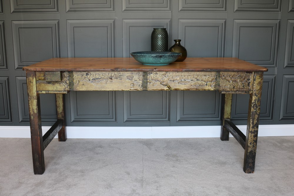 A rectangular rustic farmhouse table featuring a polished natural pine top and a heavily distressed green painted base with square legs.