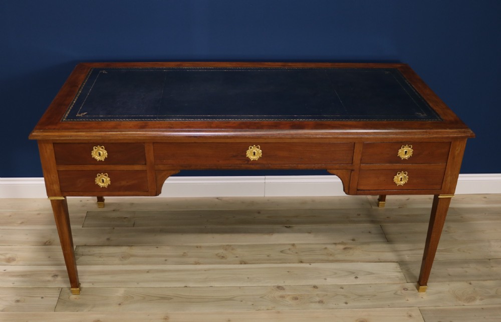 A nineteenth-century Directoire-style wooden bureau plat desk featuring five drawers with brass keyhole escutcheons, tapered legs with brass feet, and a dark leather inset writing top. View II