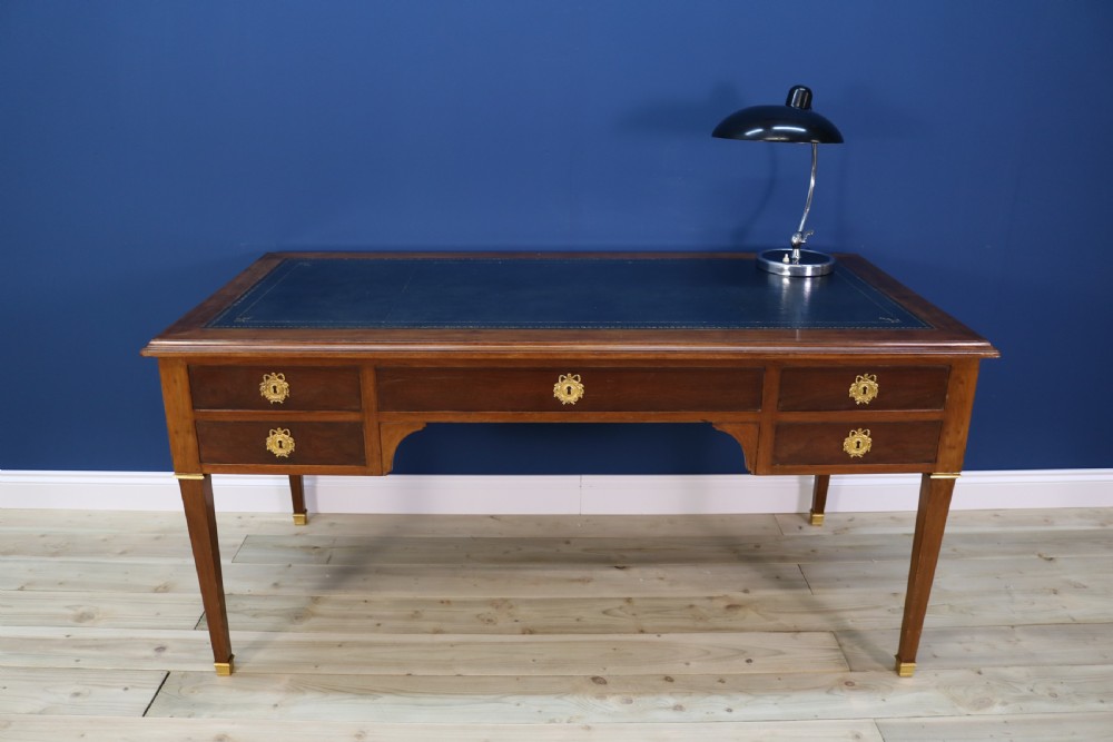 A nineteenth-century Directoire-style wooden bureau plat desk featuring five drawers with brass keyhole escutcheons, tapered legs with brass feet, and a dark leather inset writing top. View VI