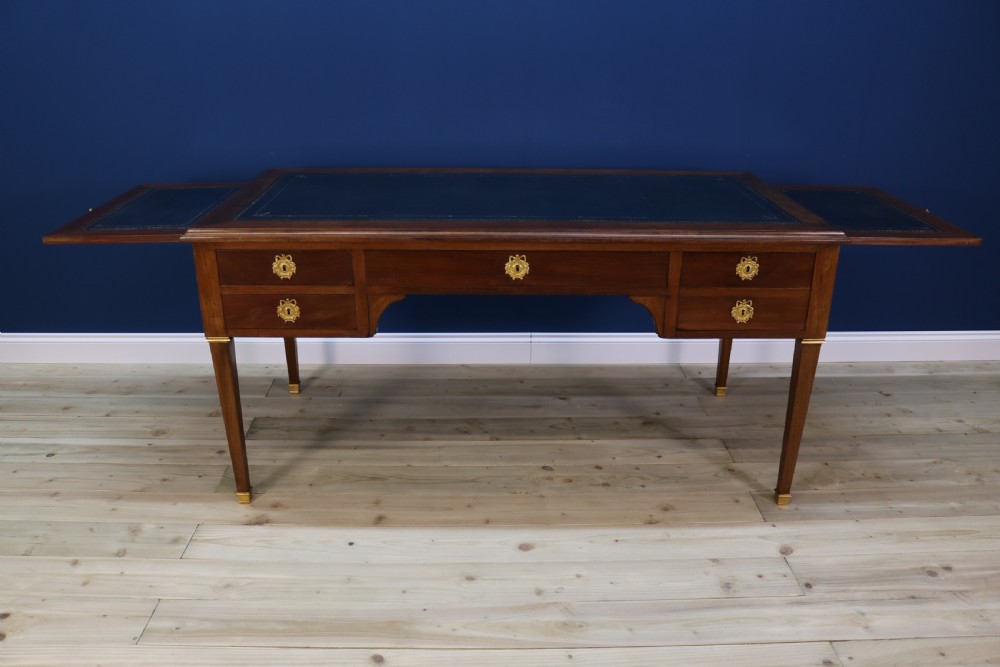 A nineteenth-century Directoire-style wooden bureau plat desk featuring five drawers with brass keyhole escutcheons, tapered legs with brass feet, and a dark leather inset writing top. View VII