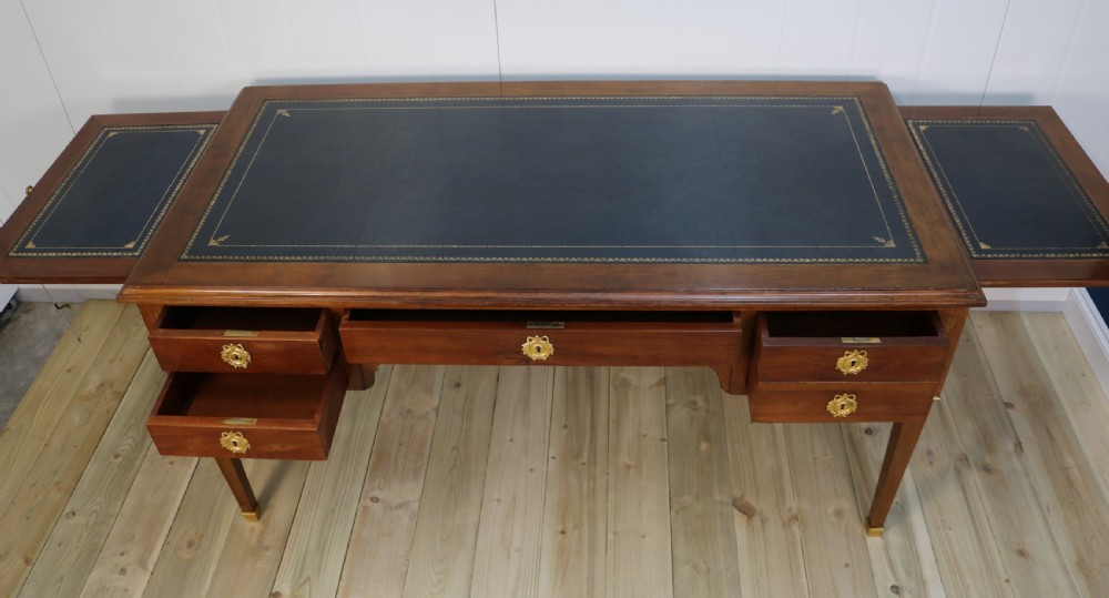 A nineteenth-century Directoire-style wooden bureau plat desk featuring five drawers with brass keyhole escutcheons, tapered legs with brass feet, and a dark leather inset writing top. View IX