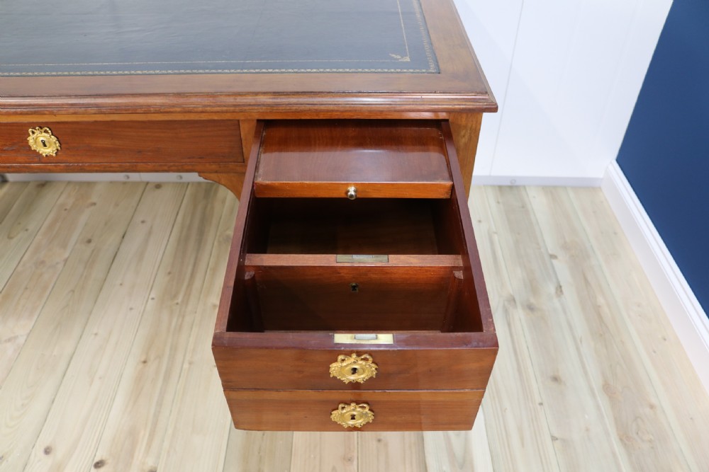 A nineteenth-century Directoire-style wooden bureau plat desk featuring five drawers with brass keyhole escutcheons, tapered legs with brass feet, and a dark leather inset writing top. View X