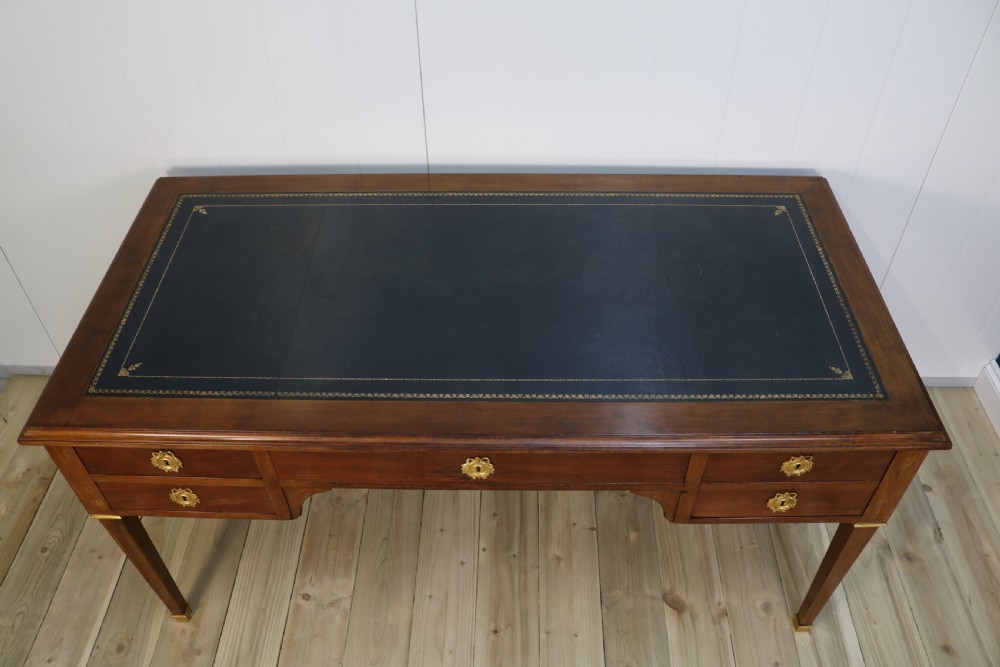 A nineteenth-century Directoire-style wooden bureau plat desk featuring five drawers with brass keyhole escutcheons, tapered legs with brass feet, and a dark leather inset writing top. View XII