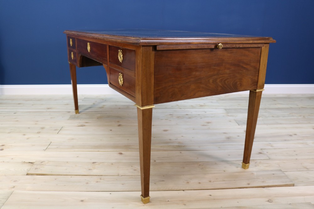 A nineteenth-century Directoire-style wooden bureau plat desk featuring five drawers with brass keyhole escutcheons, tapered legs with brass feet, and a dark leather inset writing top. View XIV