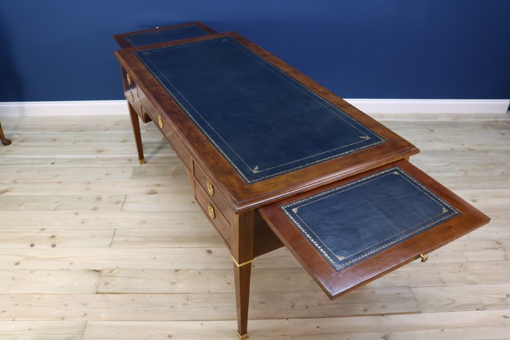 A nineteenth-century Directoire-style wooden bureau plat desk featuring five drawers with brass keyhole escutcheons, tapered legs with brass feet, and a dark leather inset writing top. View XV