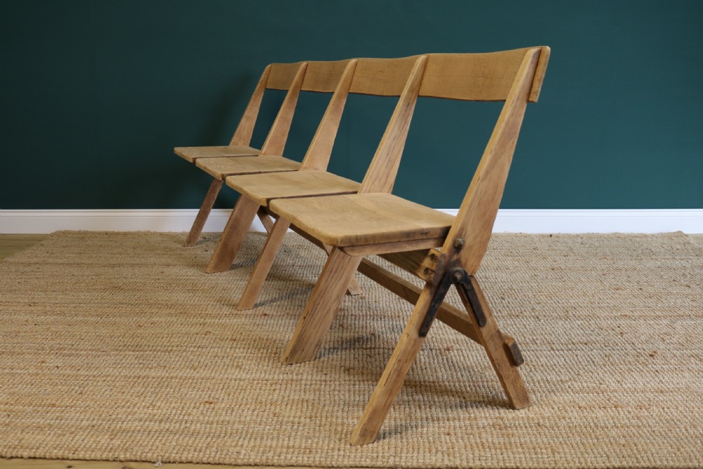 A four-seat antique folding oak bench with integrated iron hinges and sloped backrests positioned on a woven rug. View V