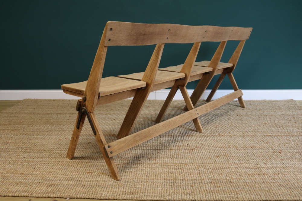 A four-seat antique folding oak bench with integrated iron hinges and sloped backrests positioned on a woven rug. View VI