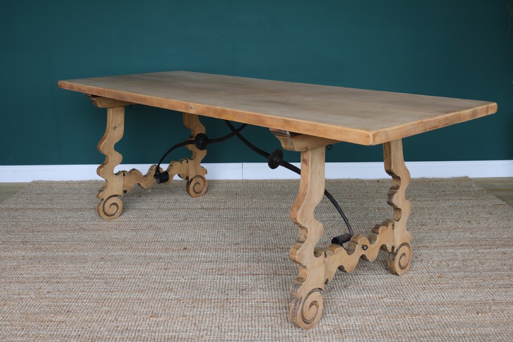 A solid walnut dining table featuring a rectangular plank top, scrolled lyre-shaped trestle legs, and curved wrought iron stretchers. View V