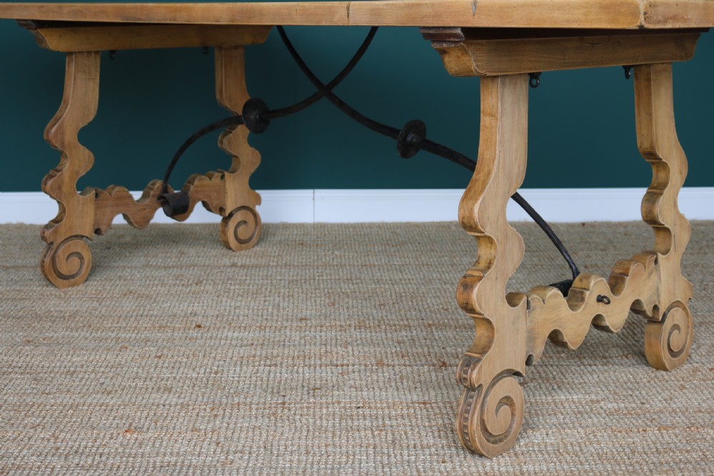 A solid walnut dining table featuring a rectangular plank top, scrolled lyre-shaped trestle legs, and curved wrought iron stretchers. View VI