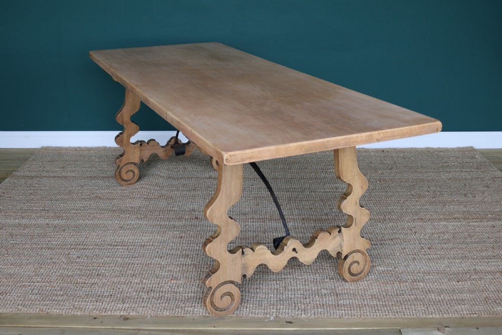 A solid walnut dining table featuring a rectangular plank top, scrolled lyre-shaped trestle legs, and curved wrought iron stretchers. View X