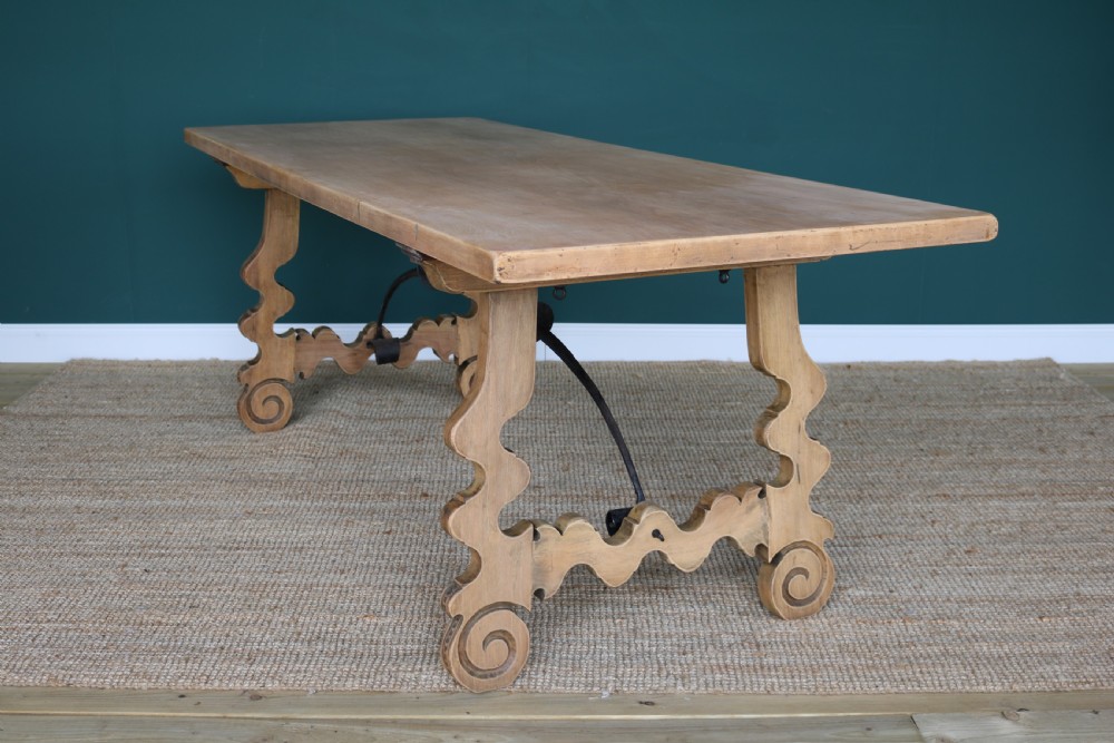 A solid walnut dining table featuring a rectangular plank top, scrolled lyre-shaped trestle legs, and curved wrought iron stretchers. View XI