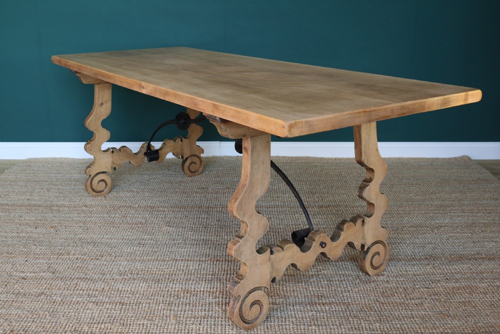 A solid walnut dining table featuring a rectangular plank top, scrolled lyre-shaped trestle legs, and curved wrought iron stretchers. View XV