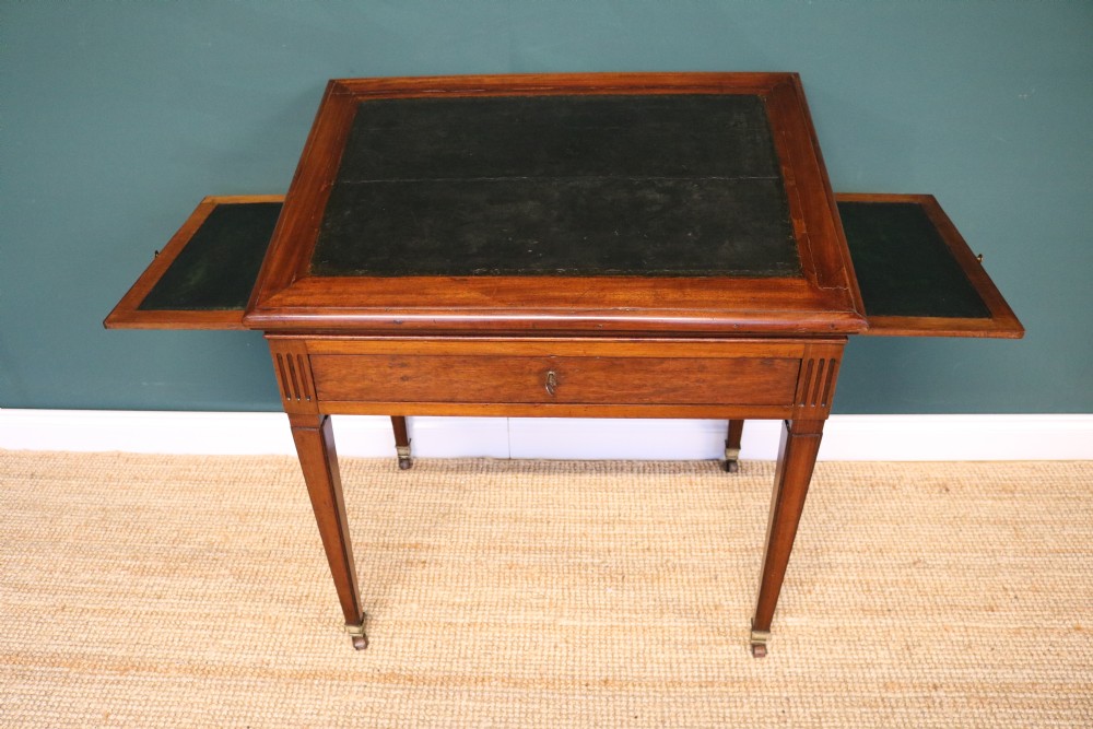 A nineteenth-century French mahogany architects desk featuring a leather inset top, single apron drawer, fluted corners, and tapered legs on brass castors. View XVI