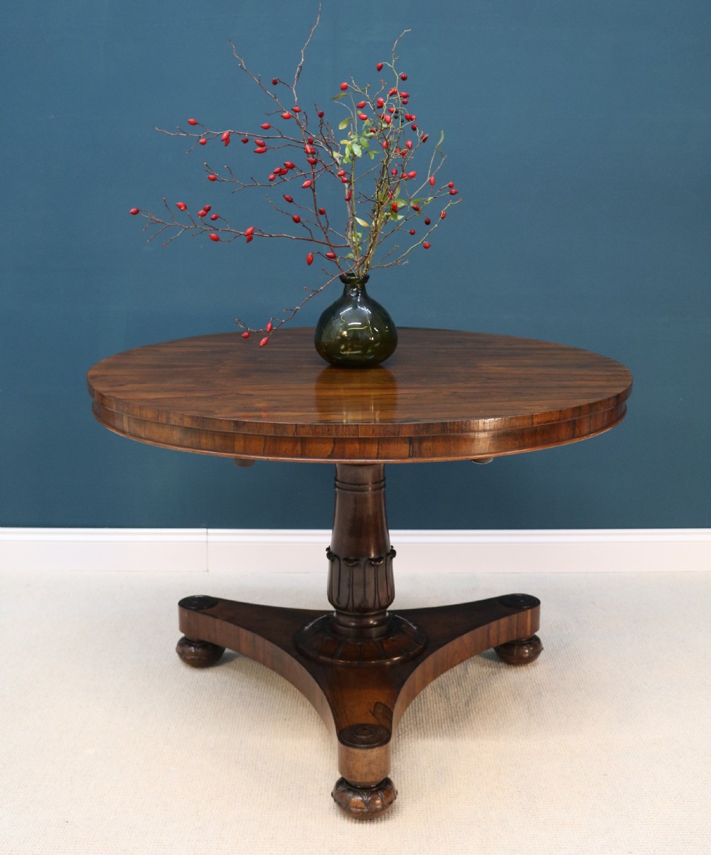 A circular 19th-century William IV rosewood centre table featuring a turned central column on a triform plinth base with carved feet.