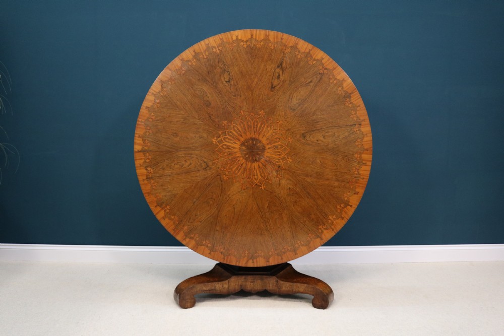 A 19th-century circular walnut centre table featuring floral marquetry inlays, a central faceted pedestal, and a tripartite platform base on scrolled feet. View VI