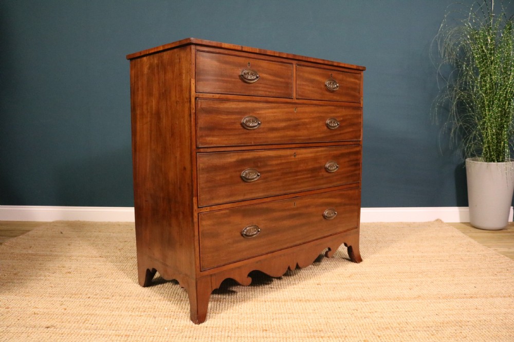 A George III mahogany chest of drawers featuring two short drawers over three long graduated drawers with brass oval handles and a decorative shaped apron.