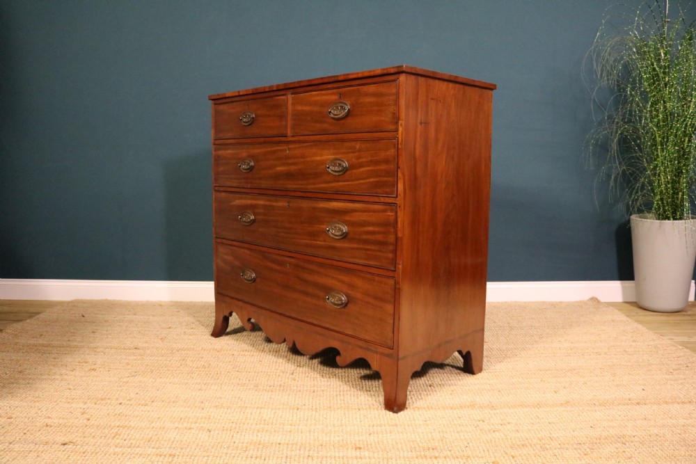 A George III mahogany chest of drawers featuring two short drawers over three long graduated drawers with brass oval handles and a decorative shaped apron. View II