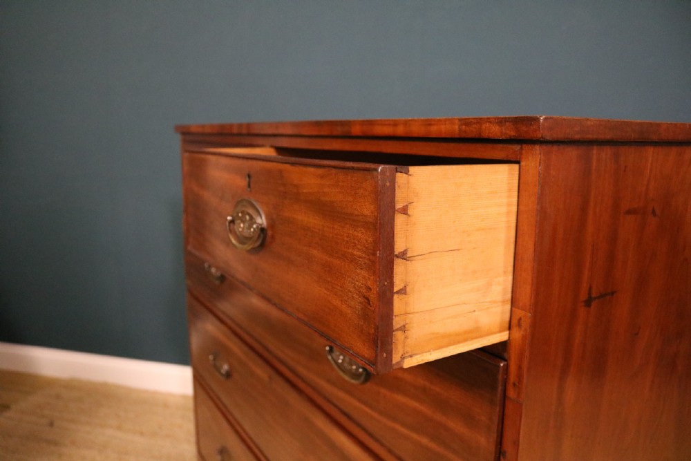 A George III mahogany chest of drawers featuring two short drawers over three long graduated drawers with brass oval handles and a decorative shaped apron. View III