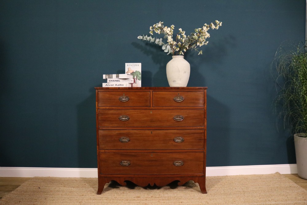 A George III mahogany chest of drawers featuring two short drawers over three long graduated drawers with brass oval handles and a decorative shaped apron. View VI