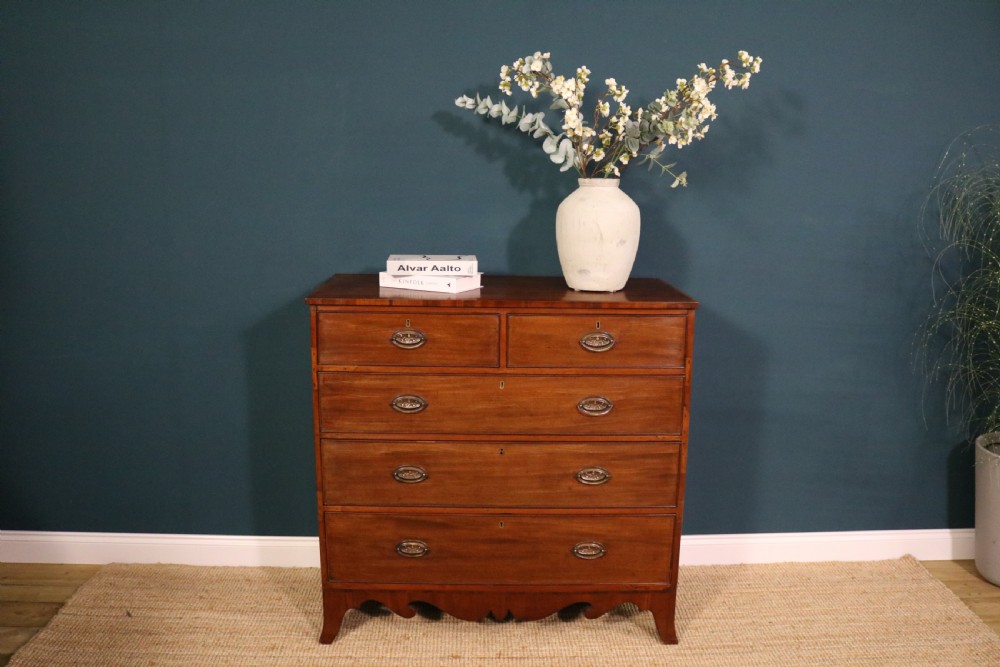 A George III mahogany chest of drawers featuring two short drawers over three long graduated drawers with brass oval handles and a decorative shaped apron. View VII