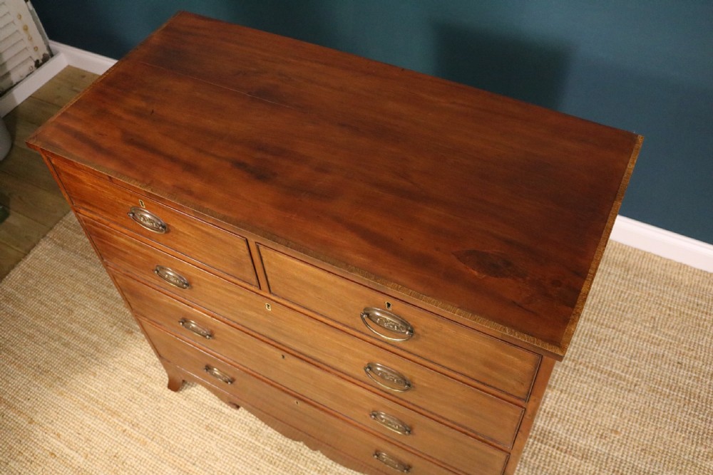 A George III mahogany chest of drawers featuring two short drawers over three long graduated drawers with brass oval handles and a decorative shaped apron. View IX