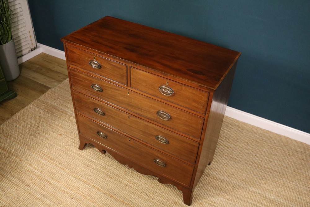 A George III mahogany chest of drawers featuring two short drawers over three long graduated drawers with brass oval handles and a decorative shaped apron. View X