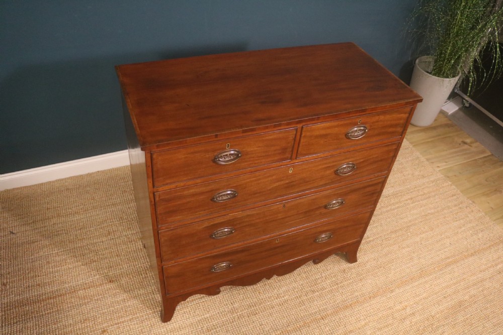 A George III mahogany chest of drawers featuring two short drawers over three long graduated drawers with brass oval handles and a decorative shaped apron. View XI