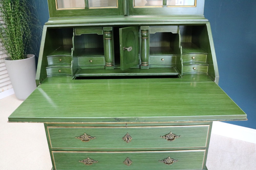 A green painted secretaire writing cabinet featuring an arched glazed upper display section, a fall-front desk revealing fitted compartments, three lower drawers with brass handles, and a matching upholstered chair. View V