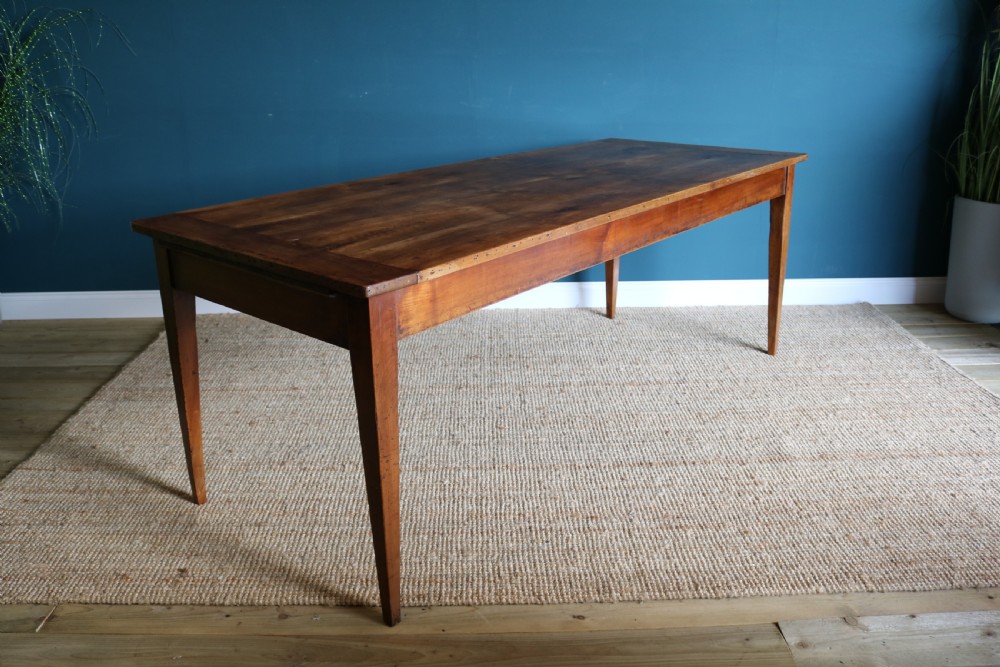 A nineteenth-century French farmhouse table constructed from warm brown cherry wood with tapered square legs and a rectangular plank top.