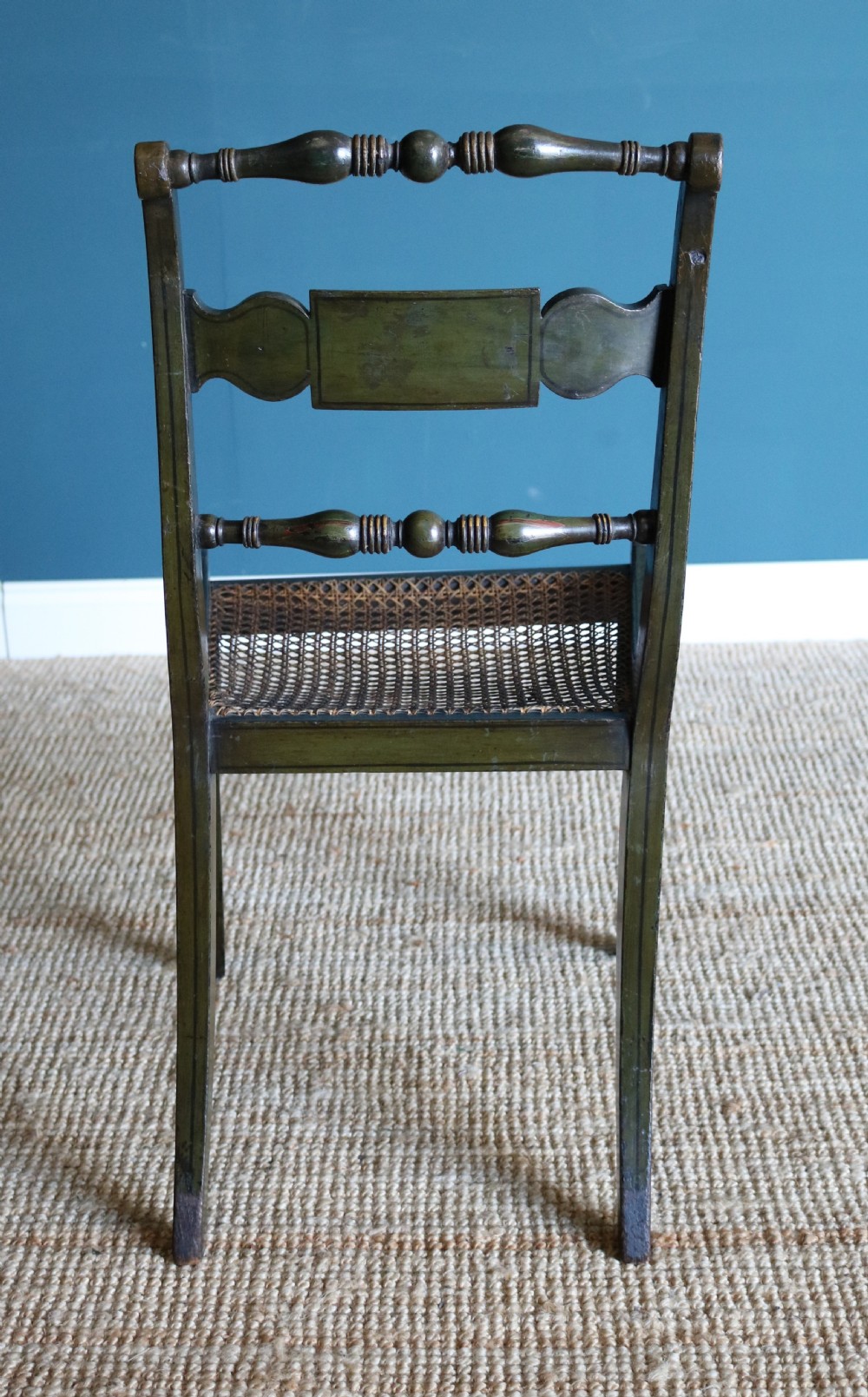 A set of six dark green hand-painted dining chairs featuring sabre legs, turned top rails, painted splats, and woven cane seats. View II