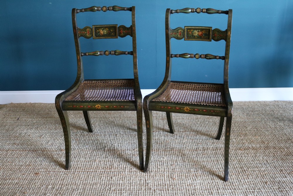 A set of six dark green hand-painted dining chairs featuring sabre legs, turned top rails, painted splats, and woven cane seats. View IX
