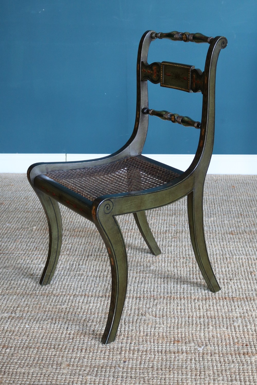 A set of six dark green hand-painted dining chairs featuring sabre legs, turned top rails, painted splats, and woven cane seats. View XI
