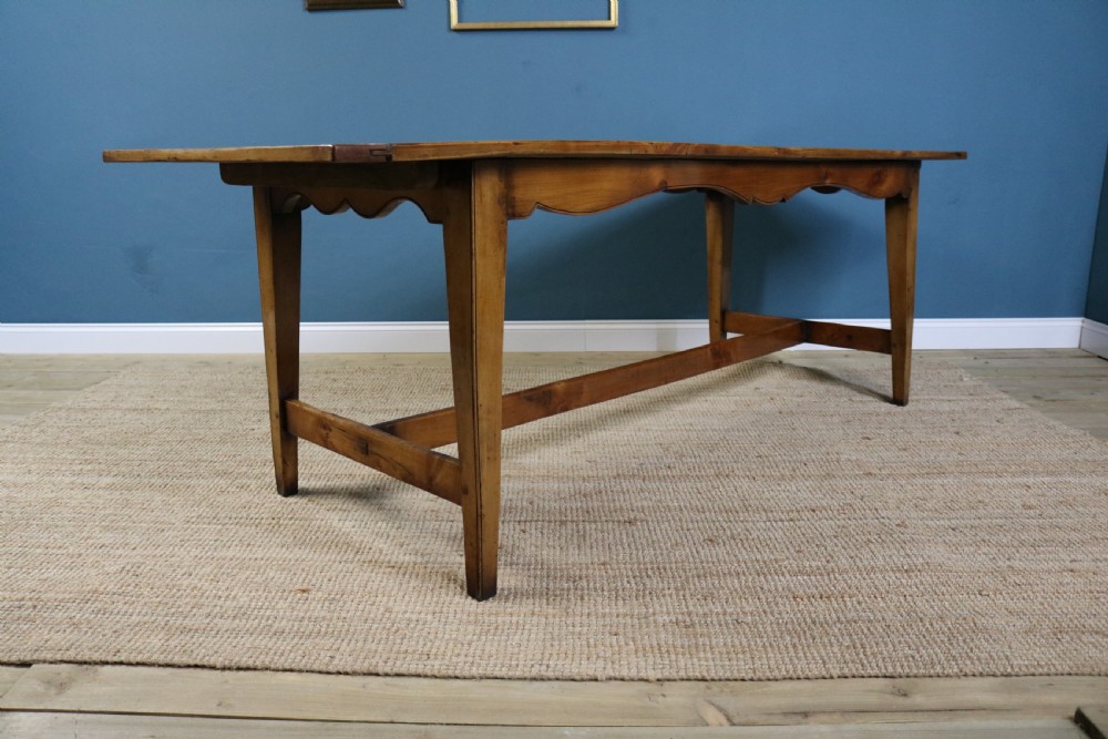 A long French cherry wood dining table featuring a scalloped apron, tapered legs, and a low stretcher base. View V