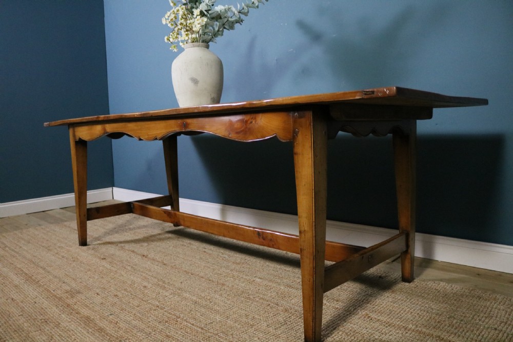 A long French cherry wood dining table featuring a scalloped apron, tapered legs, and a low stretcher base. View X