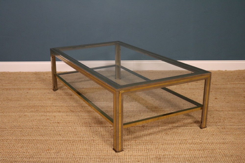 A rectangular two-tier coffee table featuring a dual-tone brass and chrome metal frame with transparent glass panels.