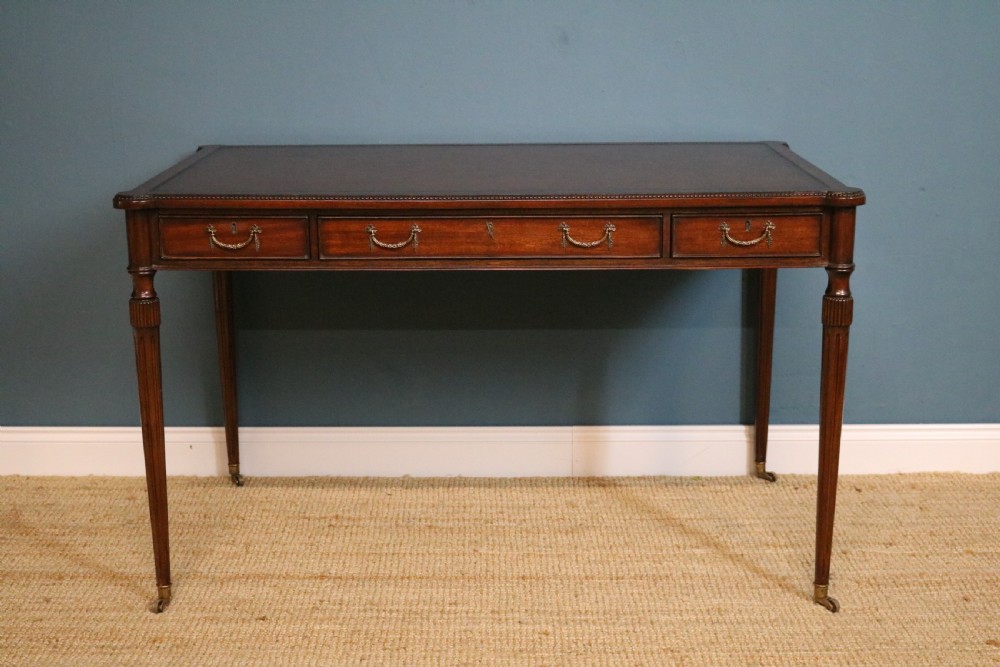 A George IV style mahogany writing table featuring frieze drawers with brass handles and reeded tapering legs on brass castors.