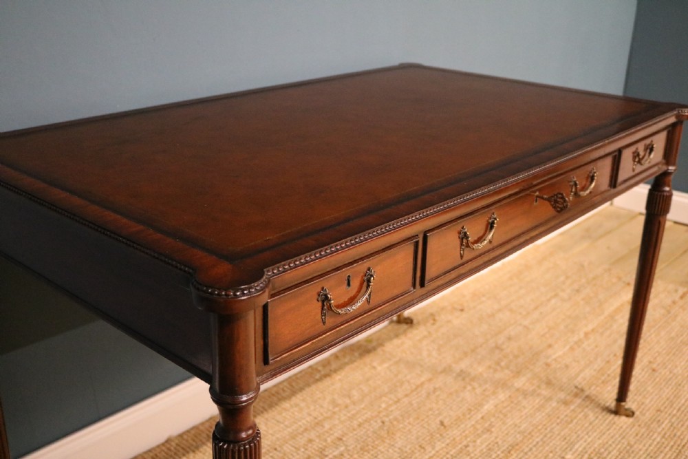 A George IV style mahogany writing table featuring frieze drawers with brass handles and reeded tapering legs on brass castors. View II