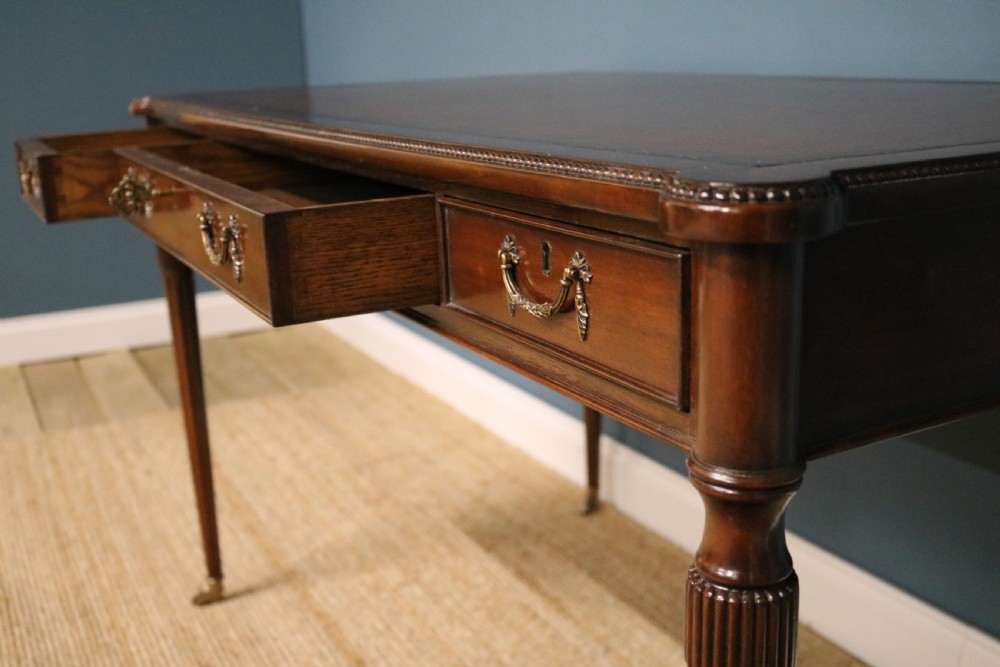 A George IV style mahogany writing table featuring frieze drawers with brass handles and reeded tapering legs on brass castors. View IV