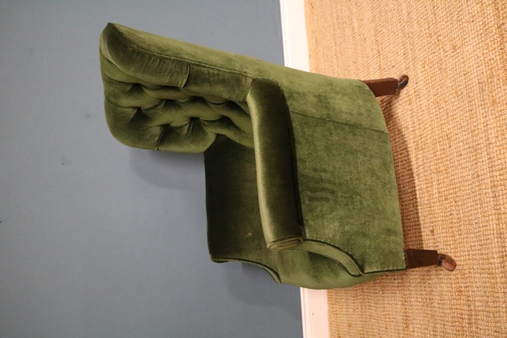 A Victorian armchair upholstered in deep forest green velvet featuring a button-backed backrest and tapered wooden front legs on castors. View V