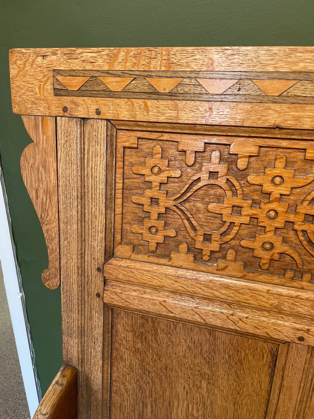 An antique Arts and Crafts solid oak settle featuring a carved high-panel back, turned legs, and a cream upholstered seat cushion. View III