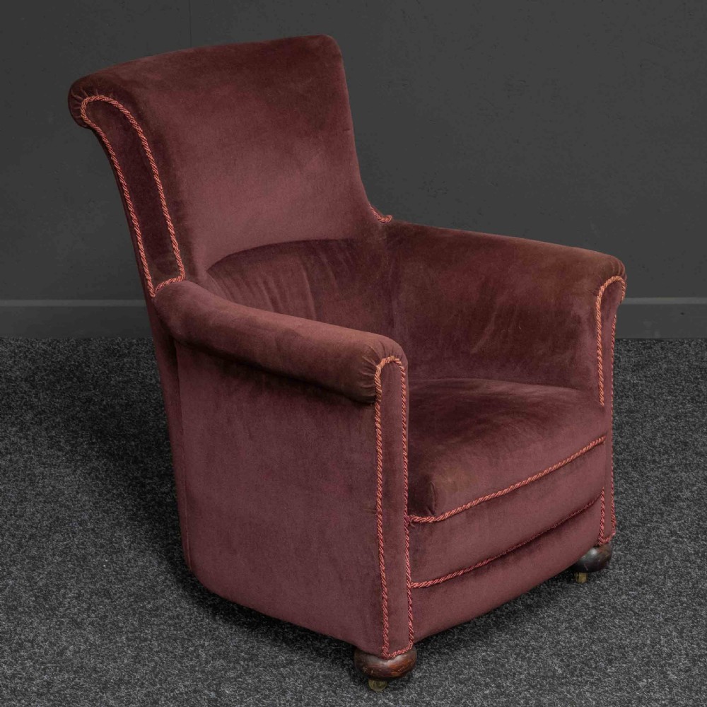 A Victorian armchair upholstered in dark burgundy velvet with braided trim detailing and short turned wooden feet on castors.