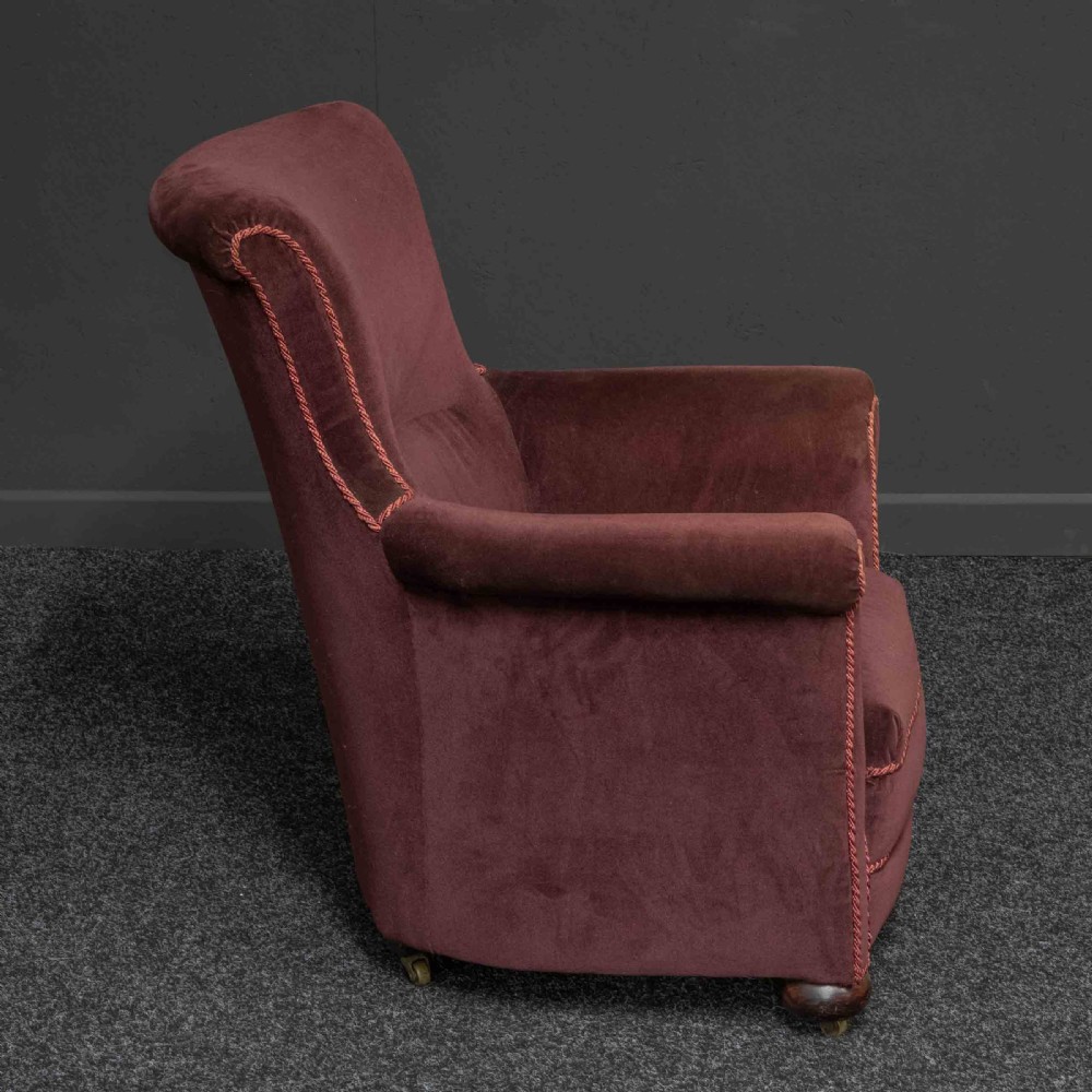 A Victorian armchair upholstered in dark burgundy velvet with braided trim detailing and short turned wooden feet on castors. View V