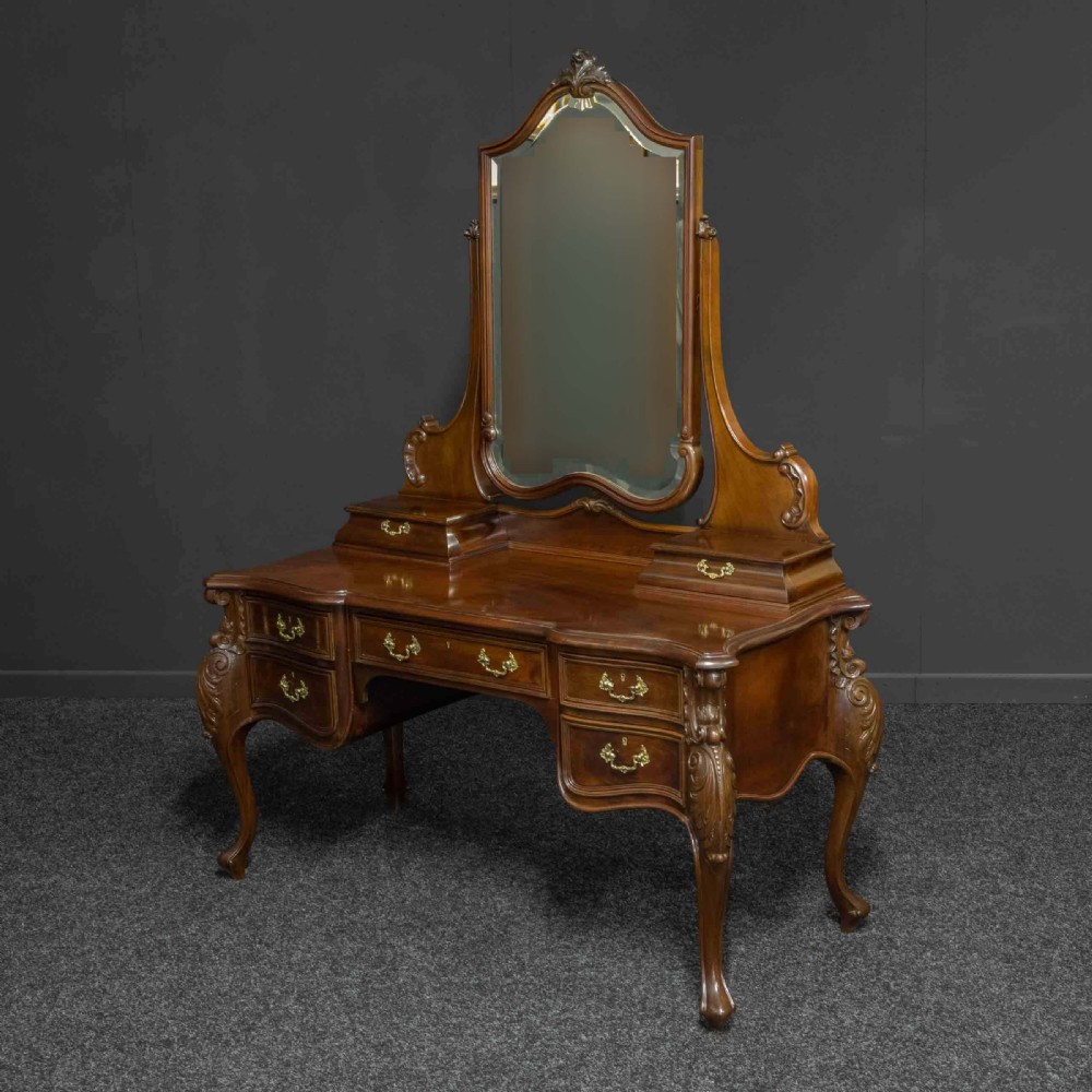 A Victorian carved mahogany dressing table featuring a central swing mirror, small upper jewellery drawers, lower storage drawers, and carved cabriole legs.